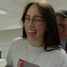 a smiling woman wearing glasses and a t - shirt in an office setting with two men