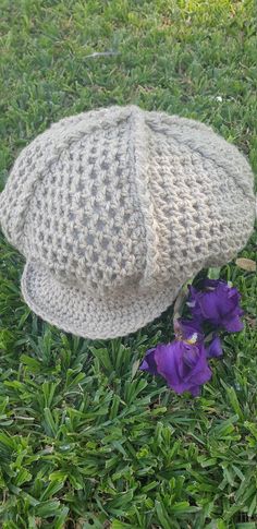 a crocheted hat laying on the grass next to purple flowers