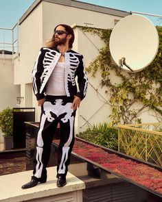 a man in a skeleton suit is standing on a ledge with his hands in his pockets