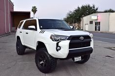 a white toyota truck parked in front of a pink building with palm trees behind it