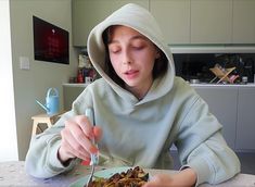 a person in a hoodie eating food at a table with a fork and knife