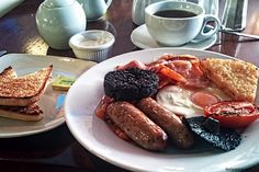 a breakfast plate with toast, sausages, tomatoes and other foods on it next to a cup of coffee