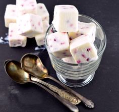 a glass bowl filled with marshmallows on top of a table next to spoons