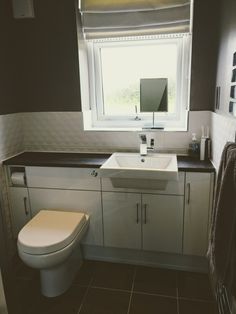 a white toilet sitting next to a bathroom sink under a window in a room with tile flooring