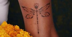 a woman's arm with a dragon tattoo on it and yellow flowers in the foreground