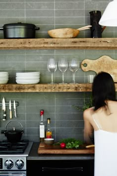 a woman standing in front of a stove top oven next to shelves filled with dishes