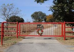 a red gate with a wreath on it is open to the road and there are trees in the background