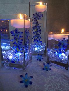 three glass vases filled with blue flowers and lit candles