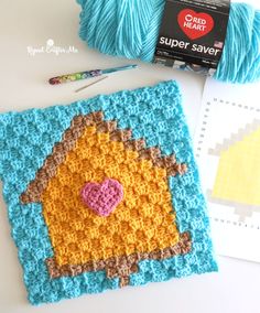 a crocheted square with a heart on it next to some yarn and scissors