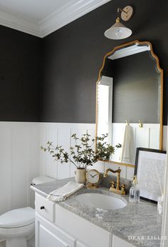 a white toilet sitting next to a bathroom sink under a mirror and a vase with flowers