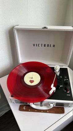 an old record player with a red vinyl record in it's case on top of a white table