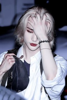 a woman with blonde hair and red eyes holding her hand to her face while wearing a white shirt