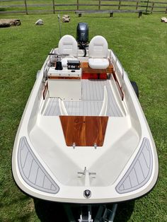 a white and brown boat sitting on top of a lush green field next to a wooden fence