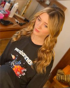 a woman with long blonde hair sitting in front of a desk and looking at the camera