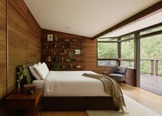 a bedroom with wood paneling and large windows overlooking the trees in the woods is shown