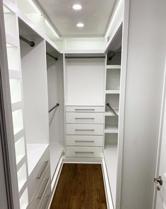 an empty walk in closet with white drawers and shelves on the wall, along with wooden flooring