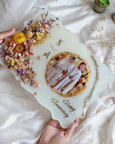 a person holding a plate with a pie on it and flowers in the middle, surrounded by other items