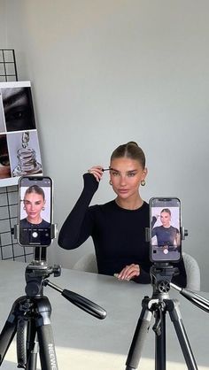 a woman sitting at a table with two cell phones in front of her and another person taking pictures