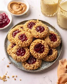 peanut butter and jelly cookies on a plate next to glass of milk, oatmeal cups and glasses