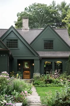 a green house with lots of flowers in the front yard and walkway leading up to it