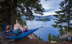 a man laying in a hammock on the edge of a cliff overlooking a lake