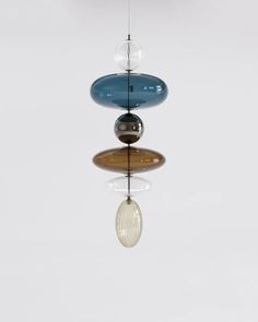 three different colored glass objects hanging from a ceiling fixture in a white room with reflections on the floor