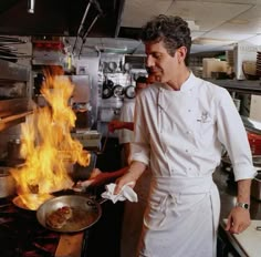 a man cooking food in a kitchen with flames coming out of the stove and on fire behind him