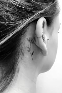 a woman's ear has a small flower tattoo on it