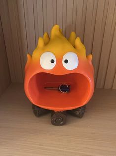 an orange and yellow toy with big eyes on top of a wooden table next to a wall