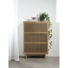 a wooden cabinet next to a window with a potted plant on top of it