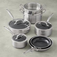 an assortment of pots and pans with lids on a gray surface, one is empty