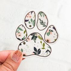 a hand holding a sticker with an animal's paw painted in floral designs