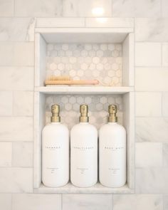 three white bottles with gold handles in a shelf above a marble tiled wall and floor