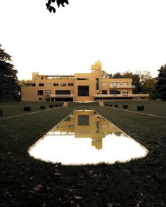 a large building that is next to some water in the middle of grass and trees