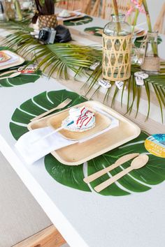 a table topped with plates and utensils next to a palm leaf covered table