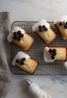 blueberry muffins with white icing and black berries on top sitting on a cooling rack