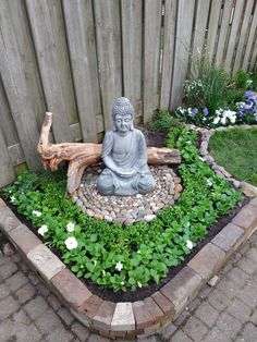 a small buddha statue sitting in the middle of a garden filled with plants and rocks