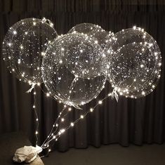 three clear balloons with lights on them are sitting in front of a black curtained background