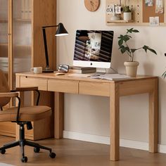 a wooden desk topped with a computer monitor next to a chair and potted plant