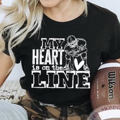 a woman holding a football and wearing a shirt that says my heart is on the line