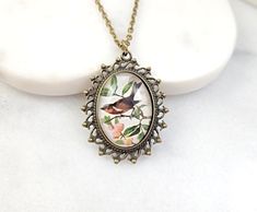 "This vintage-style bird necklace is made with an 18x25mm glass picture cabochon with a red-breasted robin perched in a rose bush. We set the cabochon in a lovely antiqued bronze bezel, and it hangs on an 18-inch antiqued bronze cable chain with a lobster clasp. This pretty necklace makes a lovely jewelry gift for her. Thank you for looking. NOTE: Gemsicles' gold-filled, rose/gold-plated, antiqued, silver and rhodium jewelry is cadmium-free, lead-free and nickel-free. Also, our plated jewelry is Bird Design Necklace Gift, Round Necklace With Bird Design For Gift, Robin Jewelry, Dove Jewelry, Rhodium Jewelry, Gifts Pink, Original Jewelry Design, Etsy Boutique, Pretty Necklace