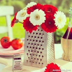 red and white flowers in a silver vase on a table next to a bottle of wine