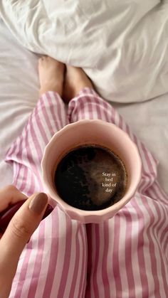 a person laying in bed holding a cup of coffee