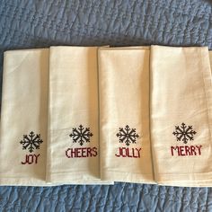 four white towels with embroidered words and snowflakes on them sitting on a bed