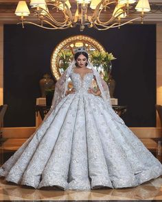 a woman in a white wedding dress standing next to a chandelier with lights on it