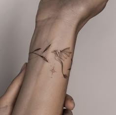 two hands holding each other with a small tattoo on the wrist that has a bird flying above it