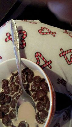 a bowl of cereal with a spoon in it on top of a table next to a pillow