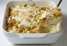 a casserole dish filled with rice, vegetables and meat in a white baking dish