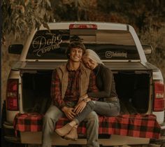 a man and woman sitting on the back of a pick up truck with their arms around each other