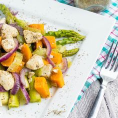 a white plate topped with asparagus, chicken and veggies next to a fork